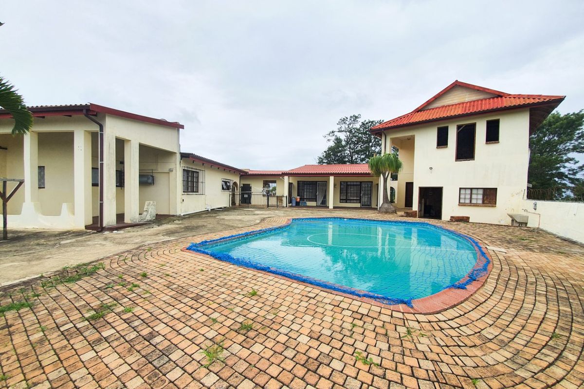 Spacious outdoor pool area featuring a paved deck, covered patio space, and multi-level building structure with tiled roofing.