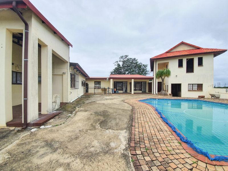 Exterior view of the pool area featuring a swimming pool, brick paving, and multiple building structures with tiled roofs.