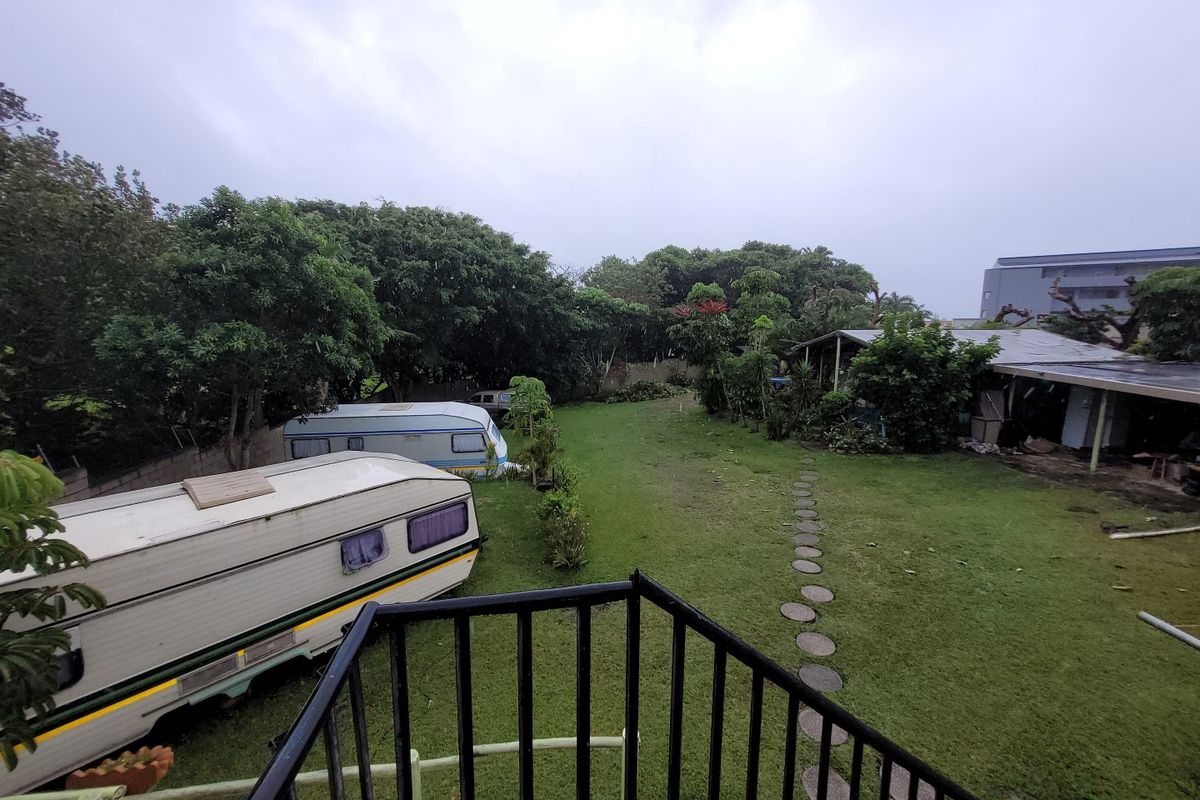A view of a large rear garden area featuring a lawn, stone pathway, and a covered outdoor structure, viewed from an elevated balcony.