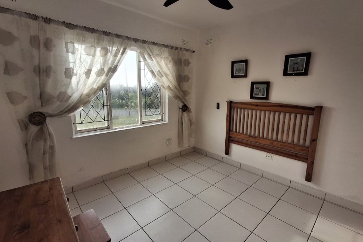 A bedroom featuring tiled flooring, a ceiling fan, and security bars on the windows. The space is ready for a modern update.