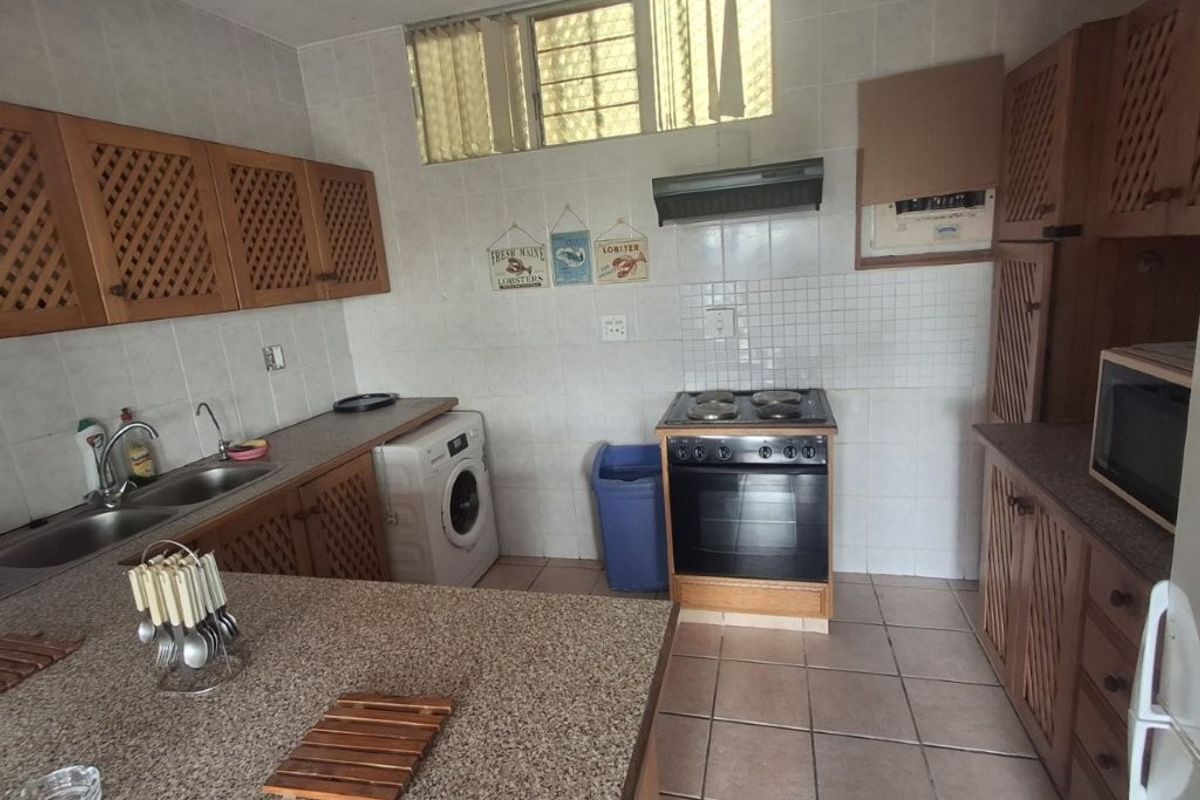 A functional kitchen featuring wooden cabinetry, tiled backsplash, double sink, and a freestanding stove with an extractor fan.