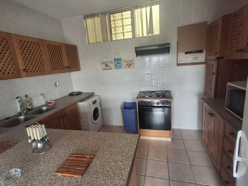 A functional kitchen featuring wooden cabinetry, tiled backsplash, double sink, and a freestanding stove with an extractor fan.