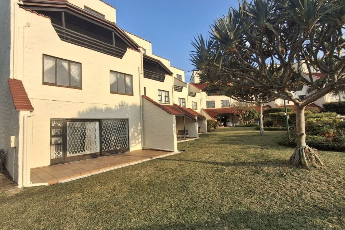 Rear view of the apartment complex featuring private tiled patios, security gates, and access to a well-maintained communal garden area.