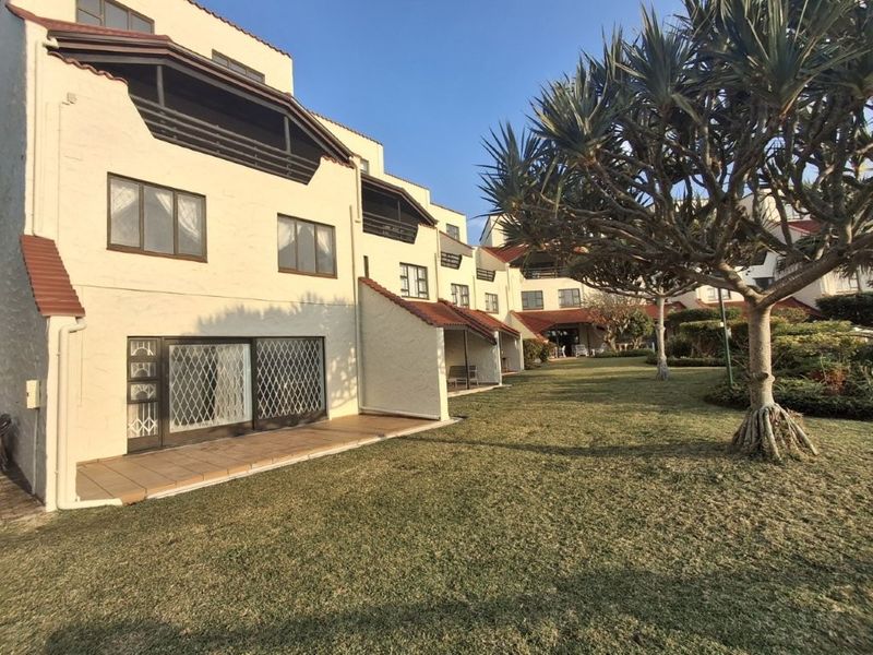 Rear view of the apartment complex featuring private tiled patios, security gates, and access to a well-maintained communal garden area.