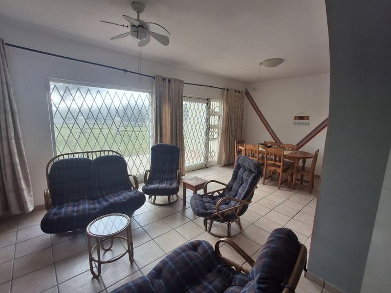 Open-plan living and dining area featuring tiled flooring, ceiling fan, and large sliding glass doors with security gates leading to the exterior.