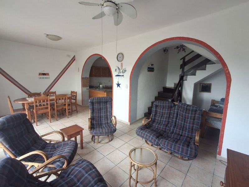 Open-plan living and dining area featuring tiled floors, arched architectural details, a ceiling fan, and an integrated staircase leading to the upper level.