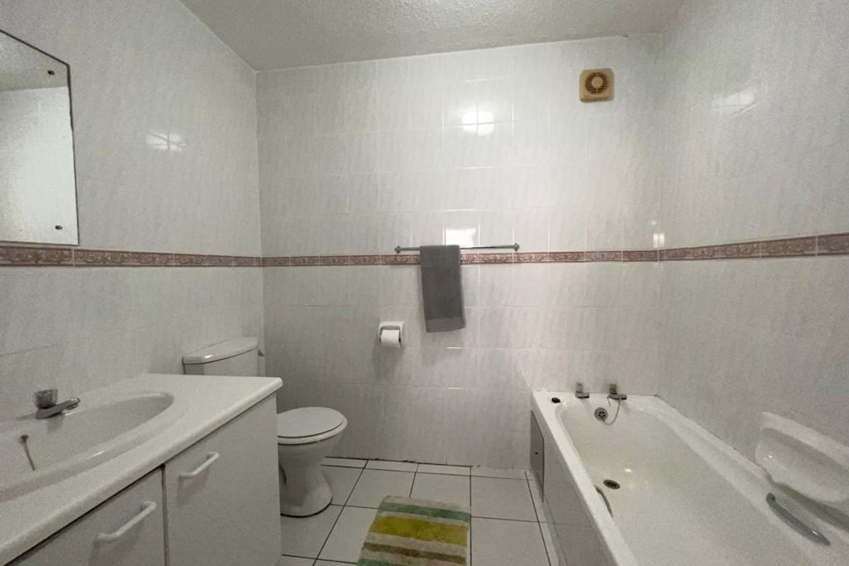 A functional bathroom featuring a vanity cabinet with integrated sink, a standard bathtub, and full-height wall tiling.