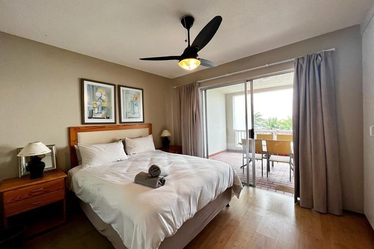 A bedroom featuring laminate flooring, a ceiling fan, and sliding glass doors that provide direct access to an outdoor balcony area.