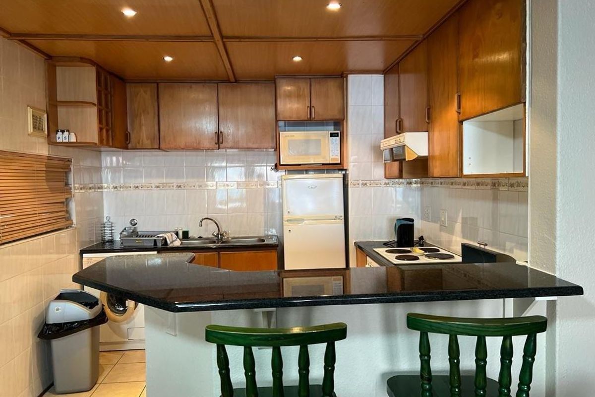 Functional kitchen featuring wooden cabinetry, granite breakfast bar, tiled backsplash, and integrated appliances, offering a practical layout for daily use.