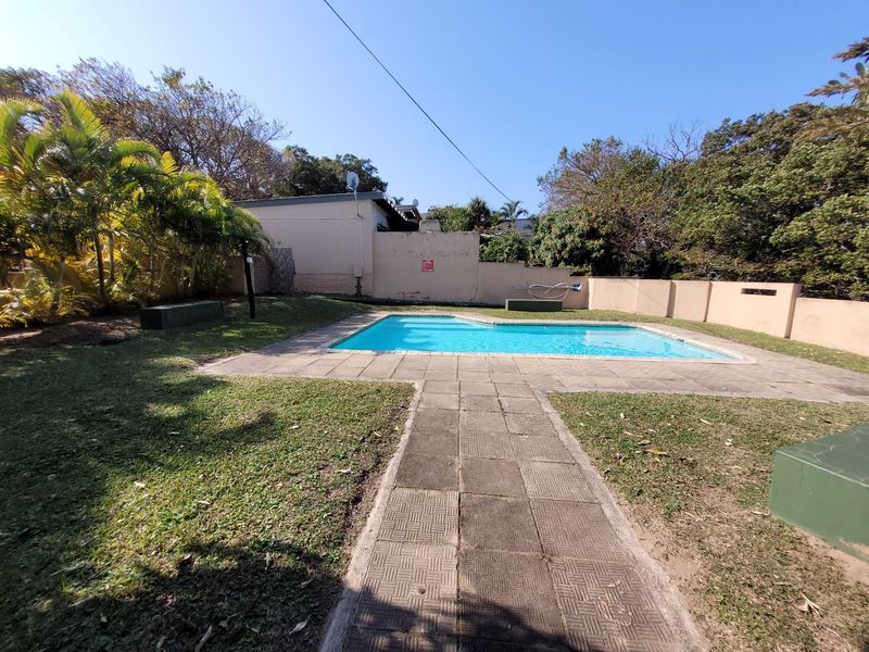 Outdoor pool area featuring a swimming pool with paved surround, lawn space, and perimeter boundary walls.