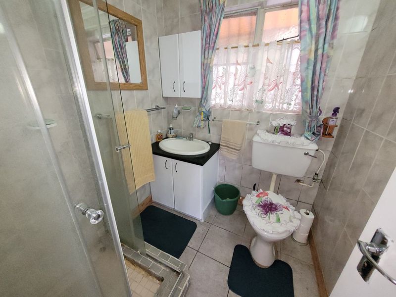 A compact bathroom featuring a shower enclosure, vanity basin, and toilet, finished with full-height wall tiling and floor tiles.