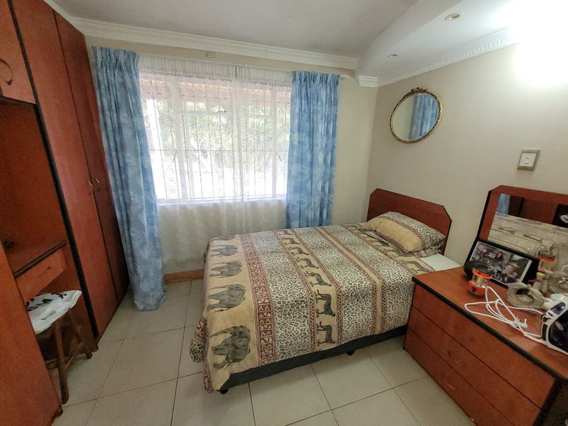 A bedroom featuring tiled flooring, built-in cupboards, and a window with natural light, offering a functional space for rest.