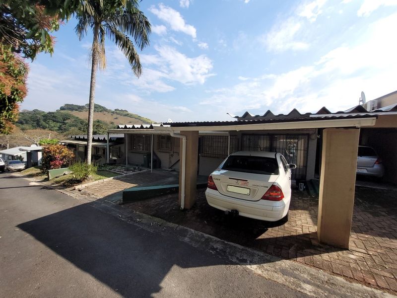 Front exterior view of the townhouse featuring a covered carport, paved driveway, and security bars on the windows.