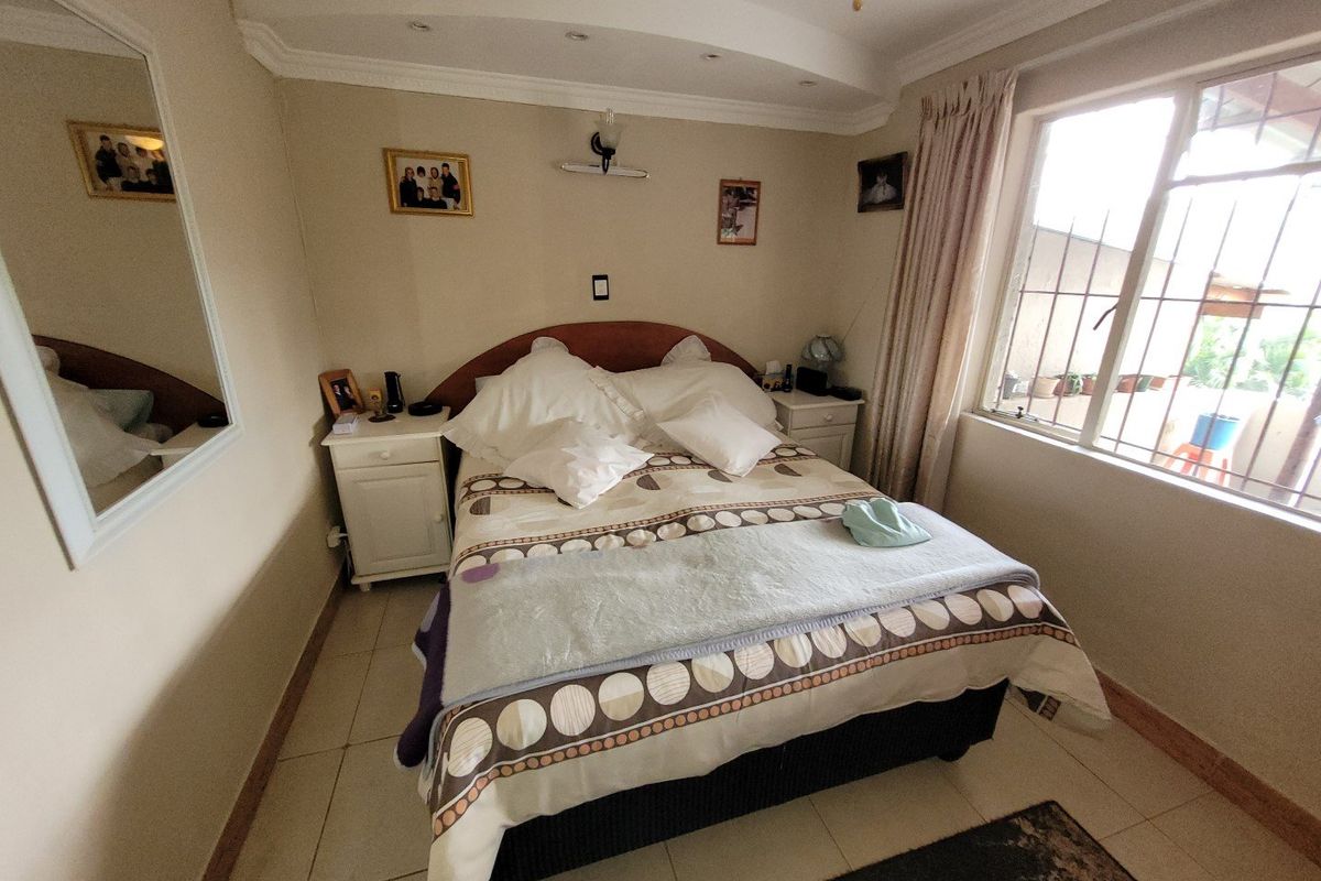 A cozy bedroom featuring tiled flooring, recessed ceiling lighting, and a window fitted with security bars.