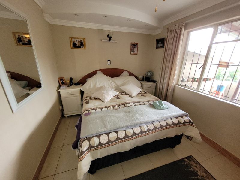 A cozy bedroom featuring tiled flooring, recessed ceiling lighting, and a window fitted with security bars.