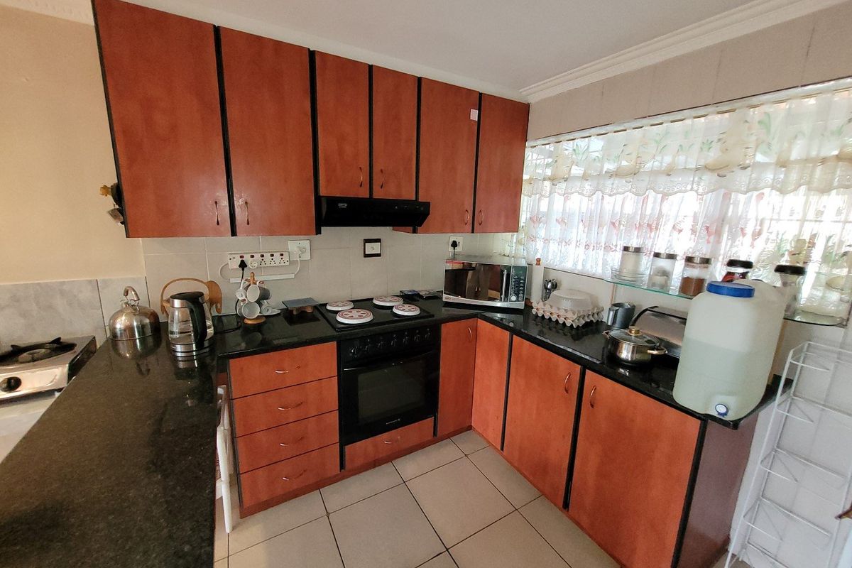 A functional kitchen featuring wooden cabinetry, granite countertops, a built-in oven with hob, and tiled flooring.