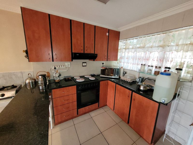 A functional kitchen featuring wooden cabinetry, granite countertops, a built-in oven with hob, and tiled flooring.