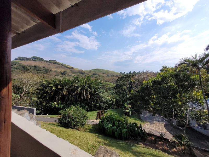 A scenic elevated view overlooking lush green hills, mature trees, and landscaped grounds from a covered patio area.