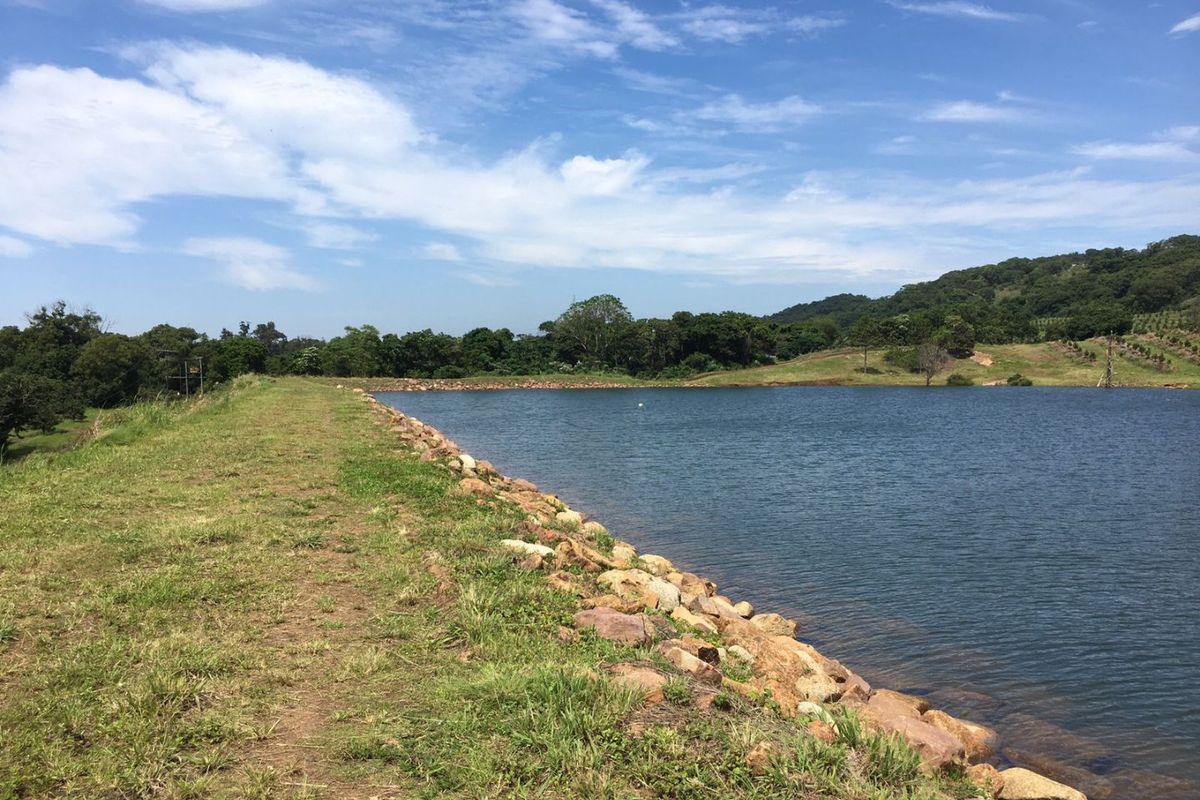 A scenic view of a farm dam featuring a stone-lined embankment and surrounding natural landscape.