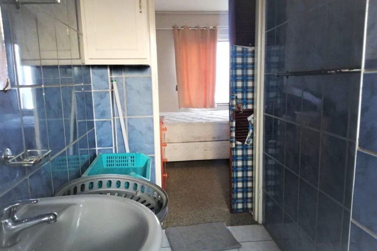 A dated bathroom featuring blue wall tiles and a pedestal basin, with a view through to an adjacent bedroom.