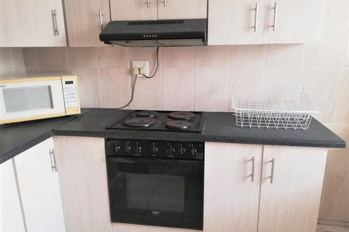 A functional kitchen featuring laminate cabinetry, a dark countertop, built-in oven, electric hob, and an extractor fan with tiled backsplash.