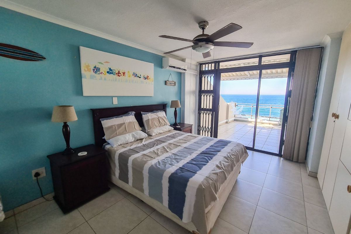 A bright bedroom featuring tiled flooring, a ceiling fan, and air conditioning, with direct access to a balcony offering expansive ocean views.