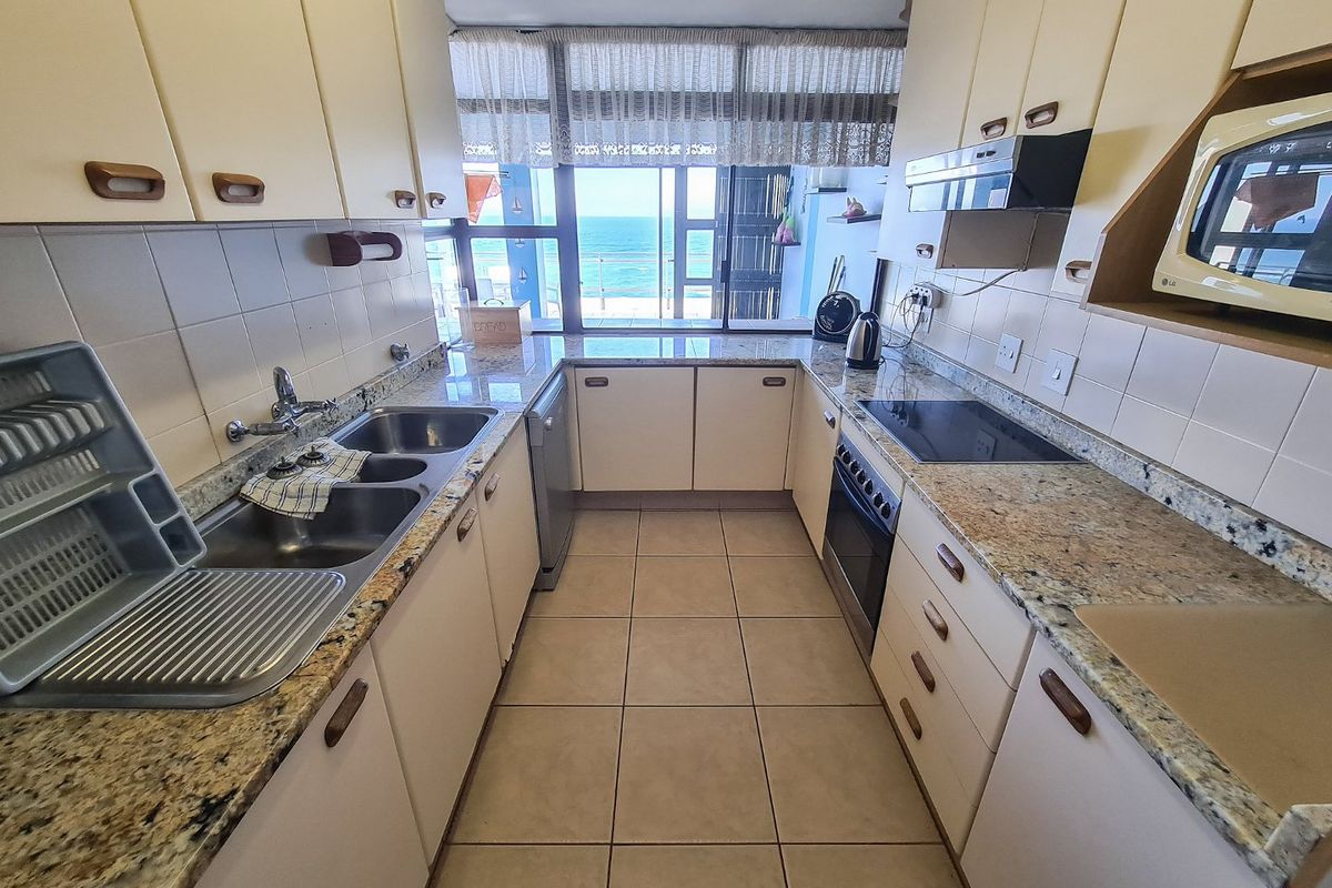 A functional galley-style kitchen featuring granite countertops, built-in cabinetry, integrated oven and hob, and a double sink, with direct views of the ocean.