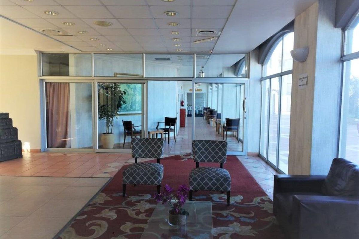 Spacious apartment building lobby or communal lounge area featuring large glass windows, tiled flooring, and a drop ceiling with recessed lighting.