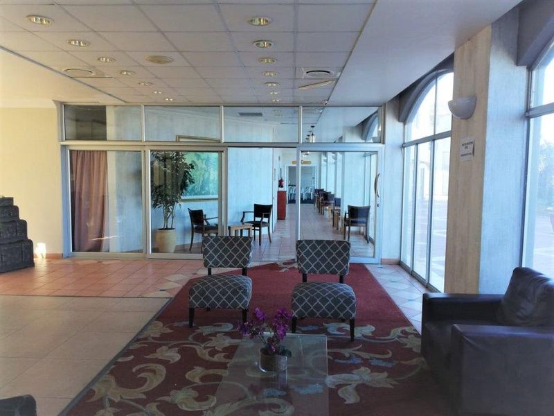 Spacious apartment building lobby or communal lounge area featuring large glass windows, tiled flooring, and a drop ceiling with recessed lighting.