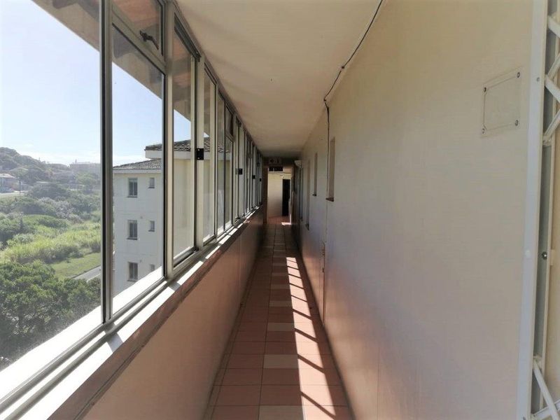 A long, enclosed apartment hallway featuring tiled flooring and a continuous row of windows overlooking the surrounding area.