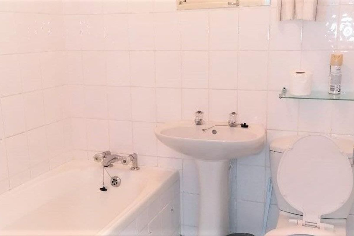 A functional bathroom featuring a white bathtub, pedestal sink, and toilet with full-height wall tiling.