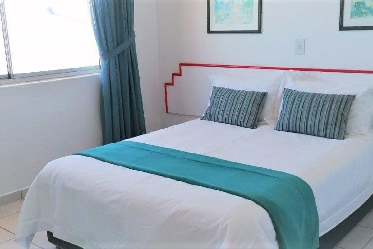 A functional bedroom featuring tiled flooring, a built-in headboard detail, and large windows allowing for natural light.