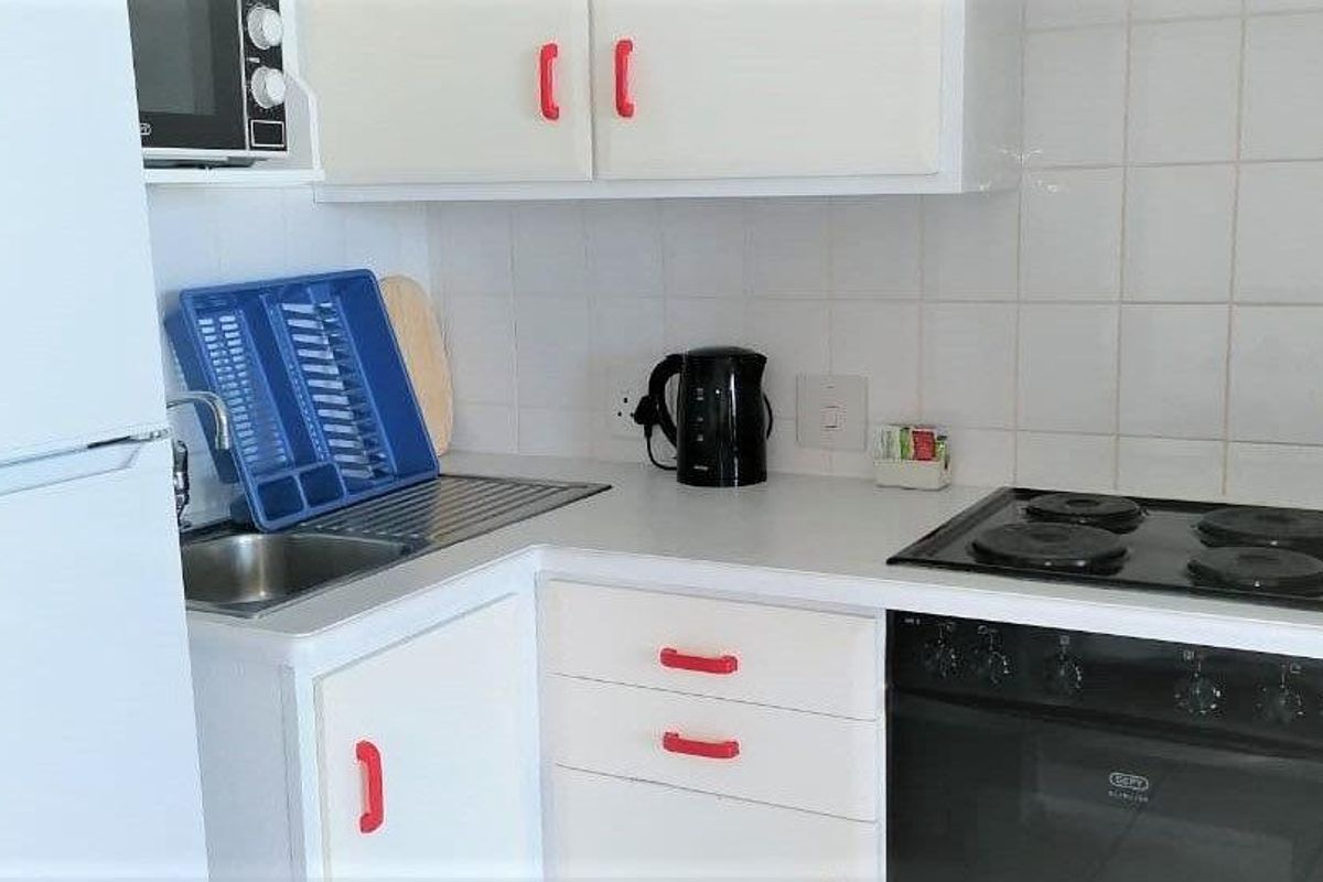 Compact kitchen featuring white cabinetry, a built-in oven with electric hob, and a stainless steel sink with tiled backsplash.