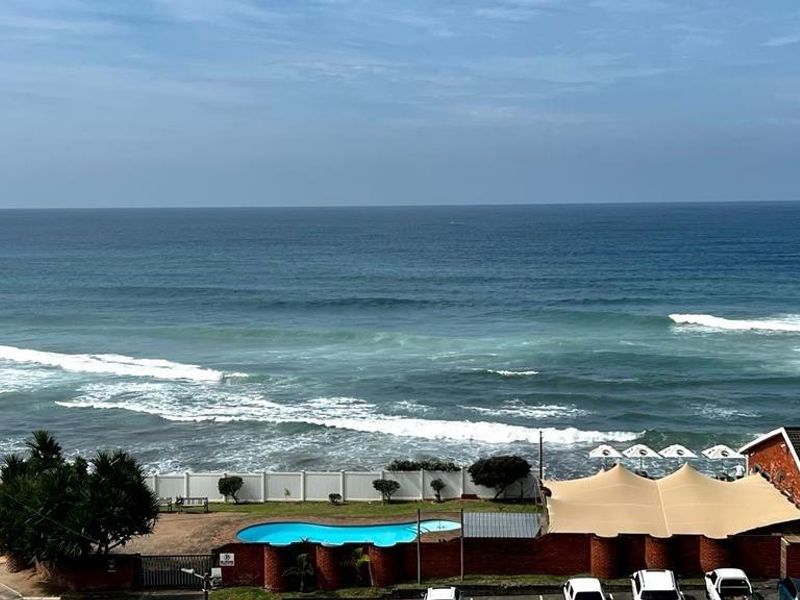 Elevated ocean view overlooking the coastline, featuring a communal swimming pool and outdoor shaded area.