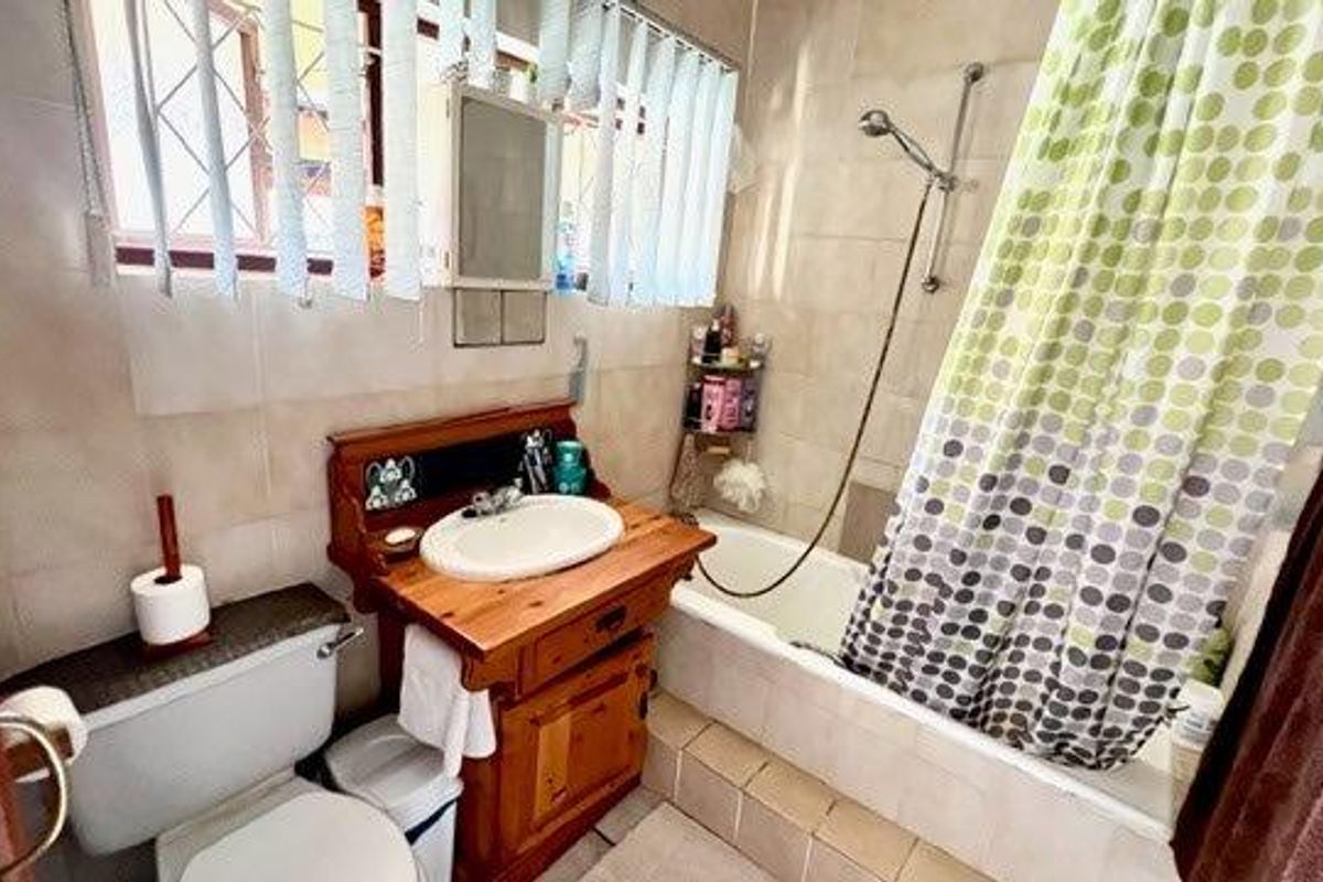 A functional bathroom featuring a built-in wooden vanity, a bathtub with shower mixer, and tiled finishes throughout.