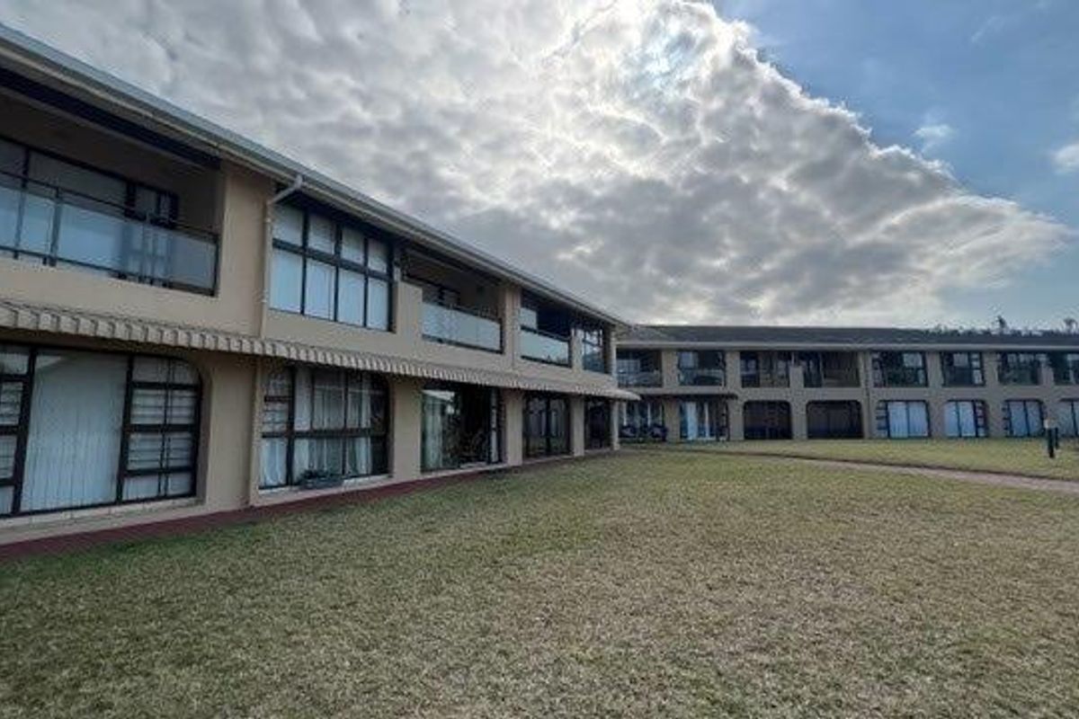 Rear view of the apartment complex featuring multiple levels with balconies, sliding glass doors, and a well-maintained communal lawn area.