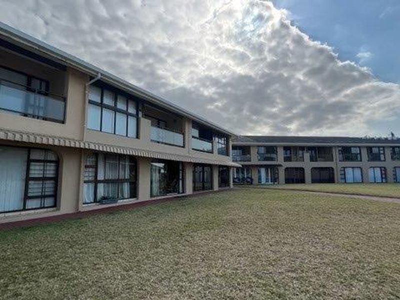 Rear view of the apartment complex featuring multiple levels with balconies, sliding glass doors, and a well-maintained communal lawn area.