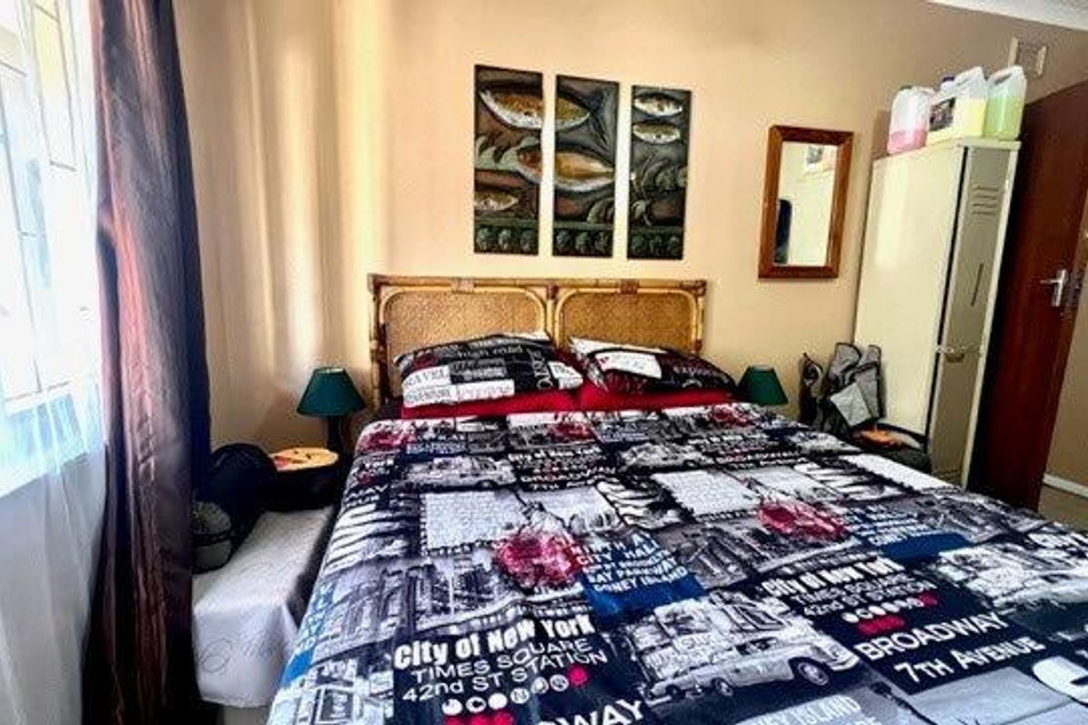 A bedroom featuring a built-in cupboard and a window fitted with security bars, providing a functional sleeping space.