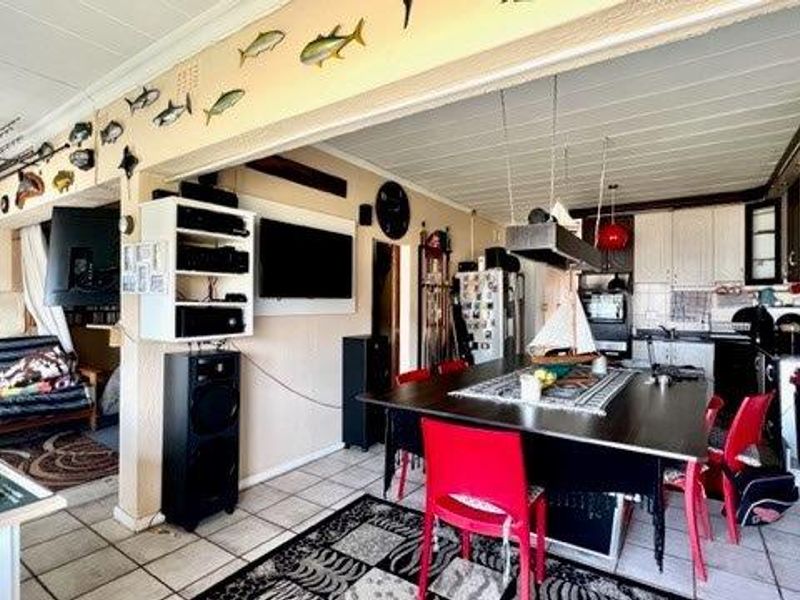 Open-plan living and dining area featuring tiled flooring and a functional kitchen with built-in cabinetry and integrated appliances.
