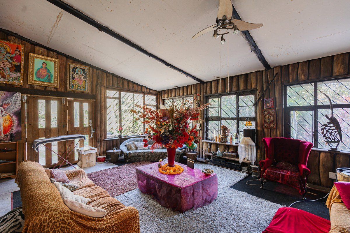 Rustic living room featuring exposed timber wall paneling, vaulted ceiling with exposed beams, and large windows with security bars.