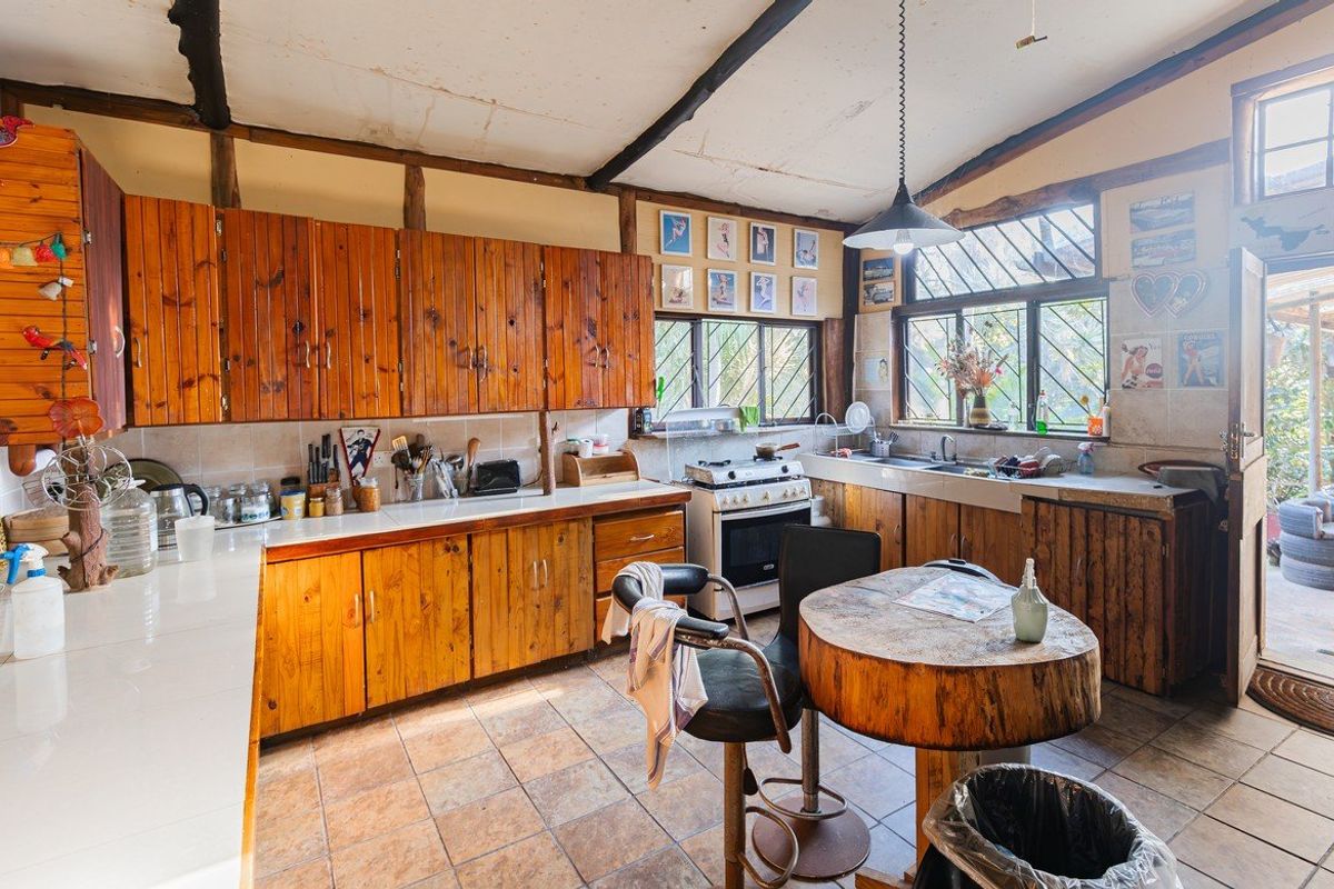 Rustic kitchen featuring wooden cabinetry, tiled countertops, a freestanding stove, and exposed timber ceiling beams, offering a traditional farmhouse aesthetic.