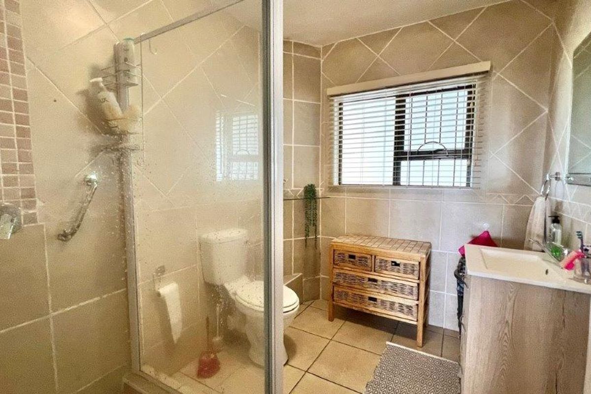 A functional bathroom featuring a glass-enclosed shower, tiled walls and flooring, a vanity basin, and a toilet with natural light from a window.