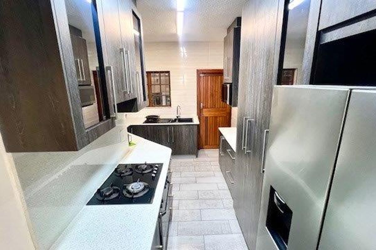 Modern galley-style kitchen featuring dark wood cabinetry, stone countertops, a gas hob, and tiled flooring with a clean, functional layout.