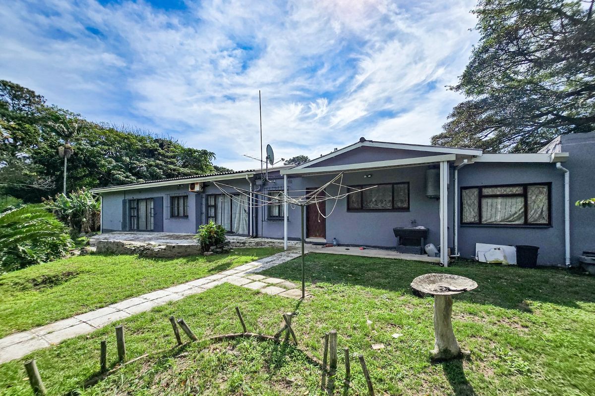 Rear view of the house featuring a covered patio area, paved walkway, and established garden space.