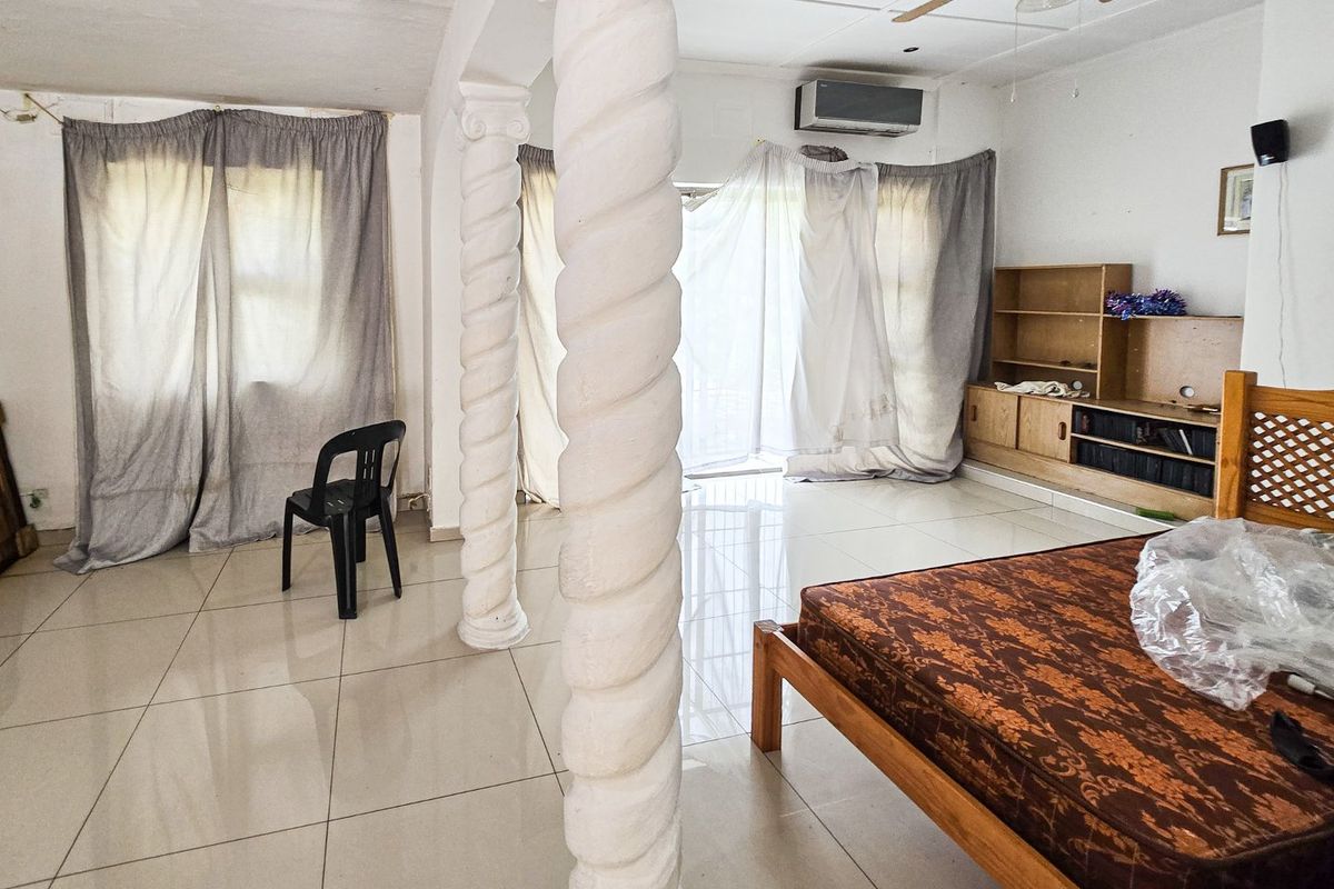 Spacious living area featuring decorative columns, tiled flooring, and a wall-mounted air conditioning unit, offering a versatile layout for customization.