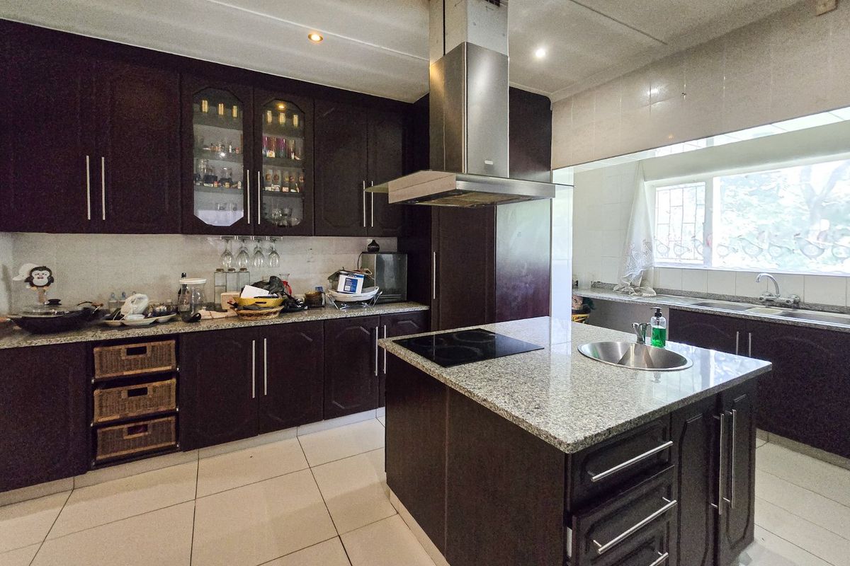 Spacious kitchen featuring dark wood cabinetry, granite countertops, a central island with a built-in hob, and a stainless steel extractor fan.