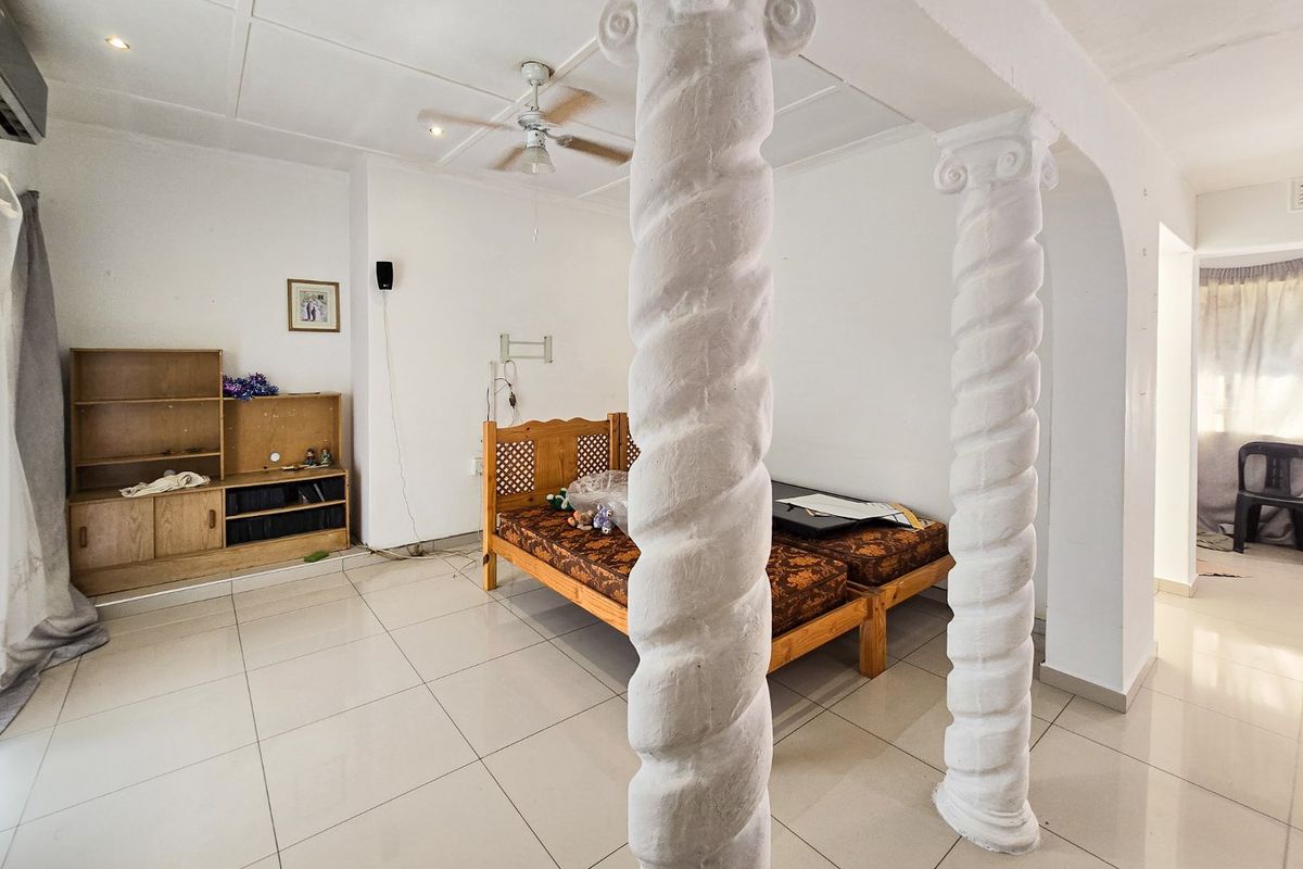 A bedroom featuring tiled flooring, decorative spiral columns, and a ceiling fan, offering a functional space with potential for modernization.