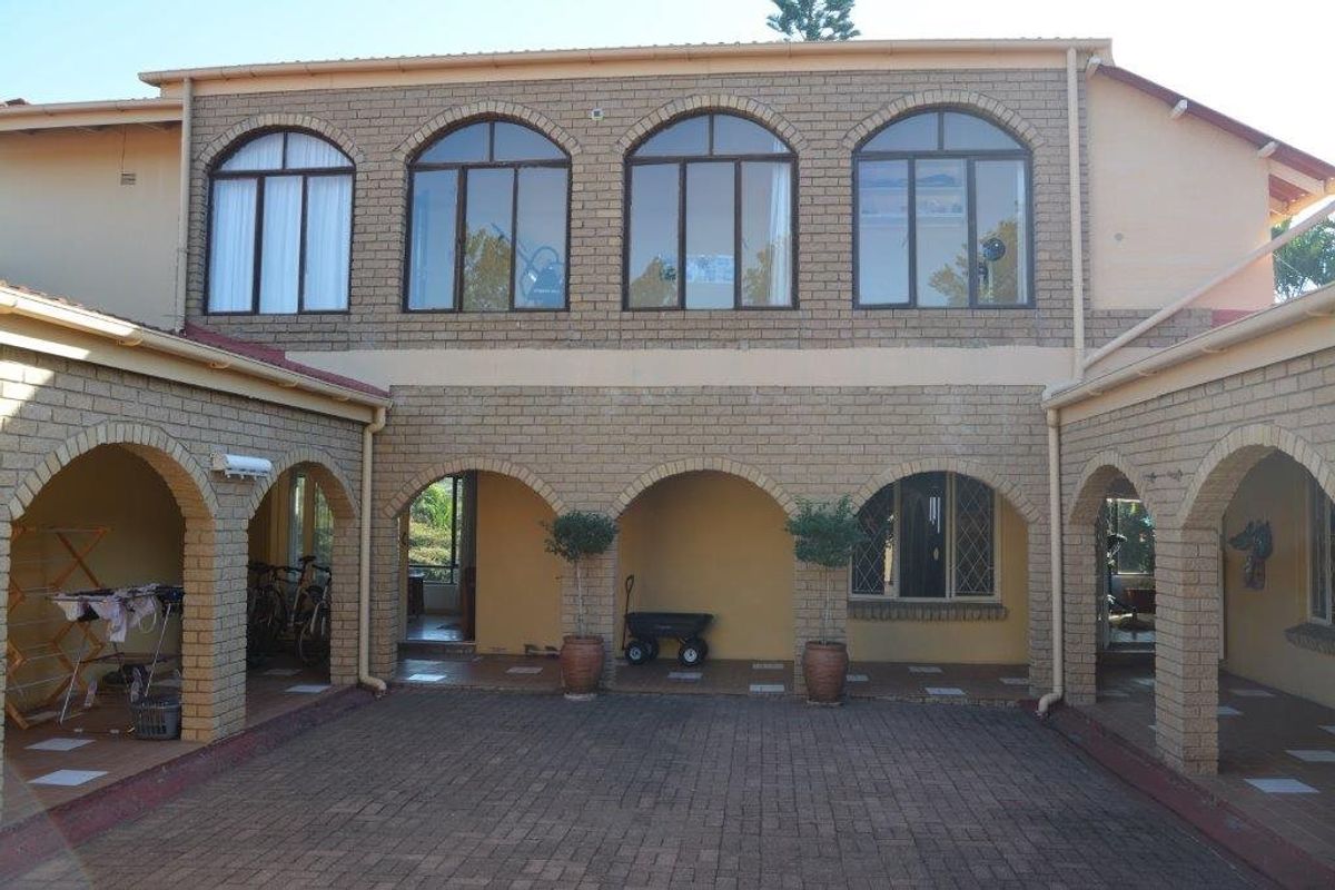 A rear view of the farm property featuring a paved courtyard, arched covered patio areas, and a two-story brick facade with arched windows.