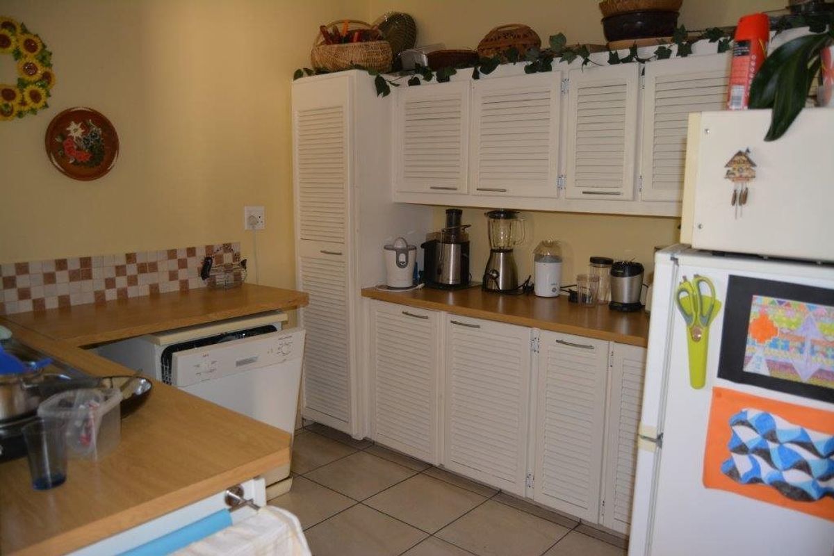 A functional kitchen featuring white louvered cabinetry, laminate countertops, and tiled flooring, offering a classic layout with ample storage space.
