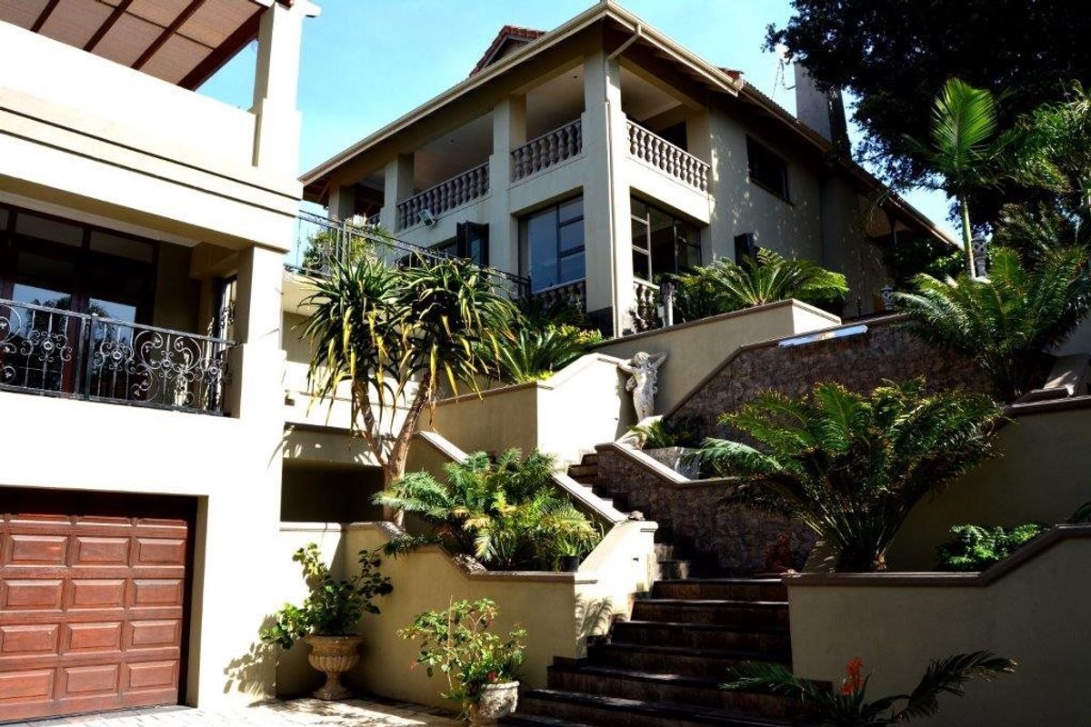 Multi-level rear exterior featuring stone-clad retaining walls, wrought iron balustrades, and a structured staircase leading to the upper terrace levels.